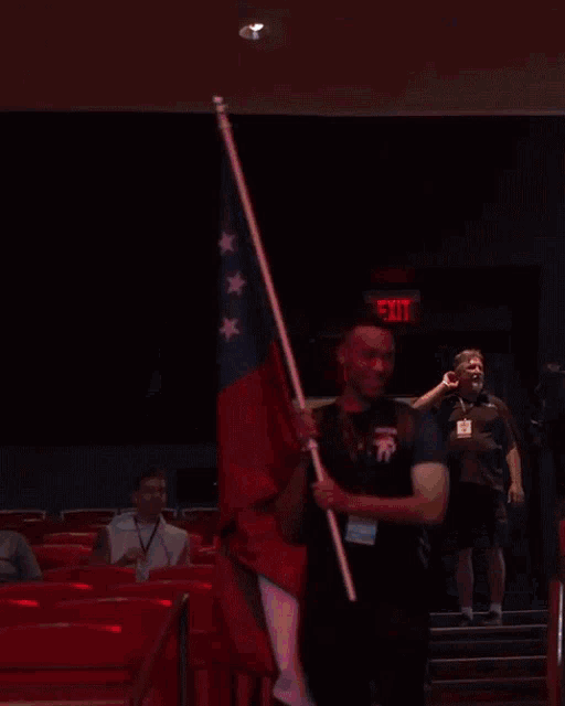 a man holding an american flag in front of a red exit sign
