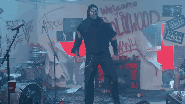 a man in a mask stands in front of a drum set in a room with graffiti on the wall