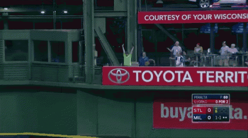 a man in a green shirt throws a baseball over a toyota sign