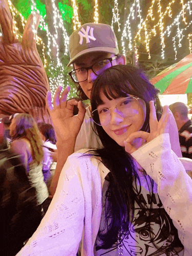 a man wearing a ny hat stands next to a girl with glasses