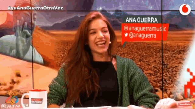 a woman in a green sweater is laughing in front of a screen that says ana guerra