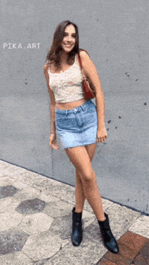 a woman wearing a crop top and a denim skirt stands in front of a wall with pika art written on it