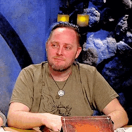 a man with a beard is sitting at a table with a book and candles in the background