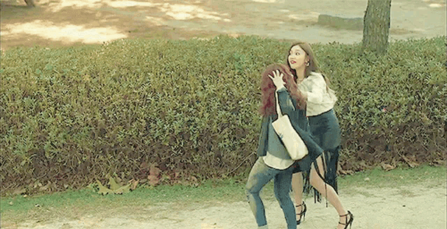 two women are standing next to each other on a dirt road in a park .