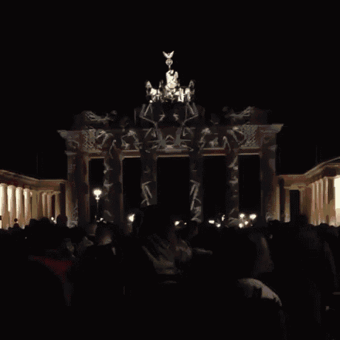 a crowd of people are gathered in front of a building that has a statue on top of it