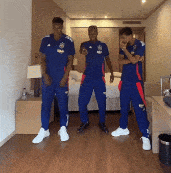three men wearing blue adidas shirts are standing in a hotel room