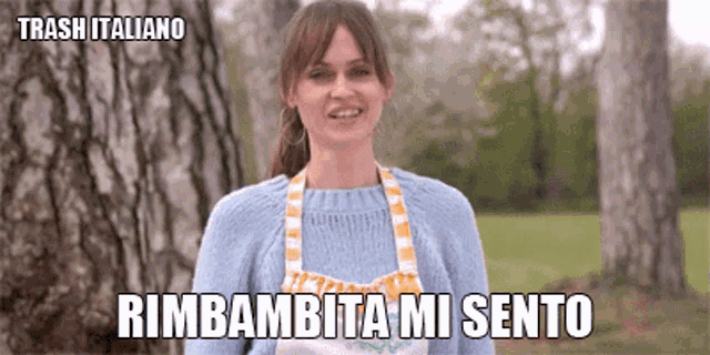 a woman wearing a blue sweater and an apron is smiling and says trash italiano