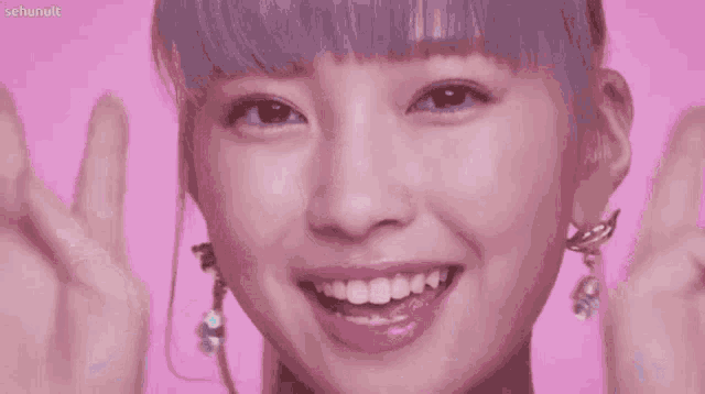 a close up of a woman 's face on a pink background giving a peace sign .