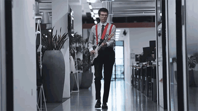 a man walking down a hallway with a guitar in his hand