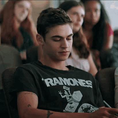 a man wearing a ramones t-shirt sits in a chair