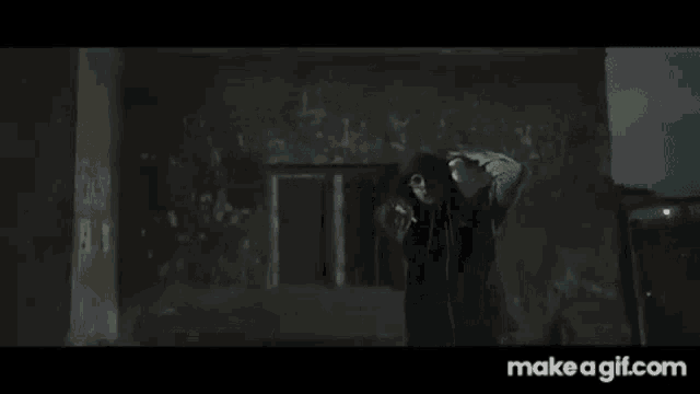 a man in a green hoodie is smoking a cigarette in a dark room with his hands on his head .
