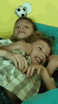 two boys laying on a bed with a soccer ball on the wall