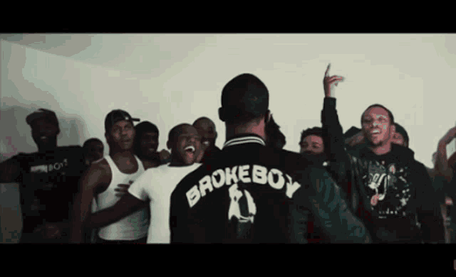 a group of men are gathered around a man wearing a jacket that says broke boy on the back