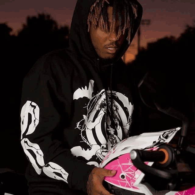 a man wearing a black hoodie holds a pink helmet