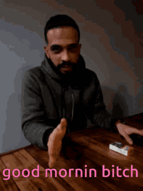 a man with a beard is sitting at a table with a cigarette in front of him and the words good mornin bitch below him