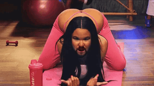 a woman with a beard is kneeling on a yoga mat next to a shake bottle that says latefit