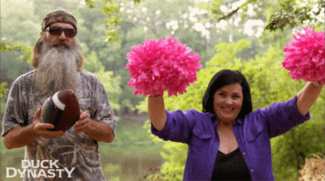 a man with a beard holds a football and a woman holds pink pom poms in front of a duck dynasty logo