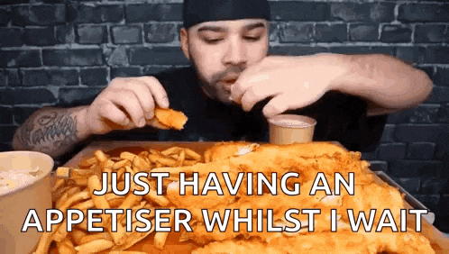 a man is sitting at a table eating a large piece of fish and fries .