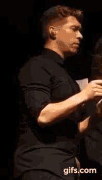a man in a black shirt is standing in front of a sign that says ' gifs.com ' on it