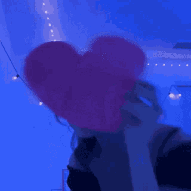 a woman is covering her face with a pink heart shaped balloon .