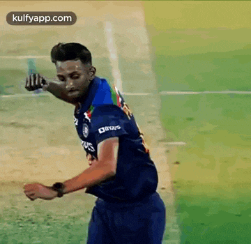 a man in a blue shirt is standing on a cricket field holding a bat .