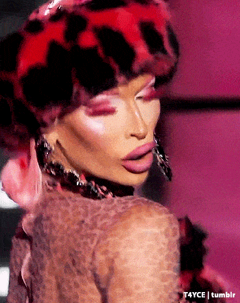a drag queen wearing a leopard print hat and earrings is looking at the camera .