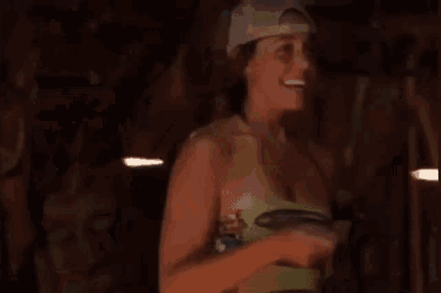 a woman is standing in a dark room wearing a hat and holding a frisbee .