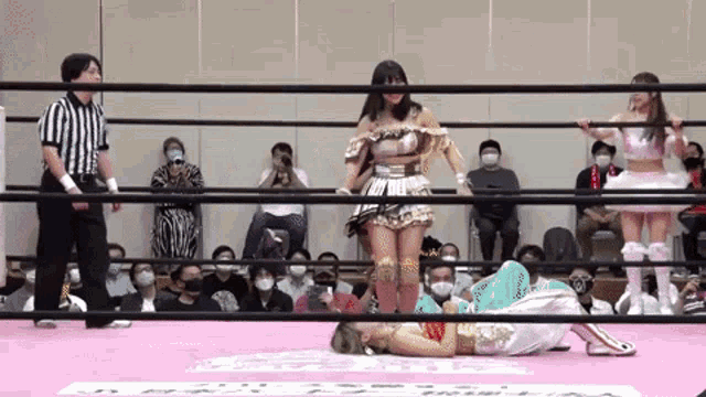 two women are wrestling in a ring while a referee stands behind them .
