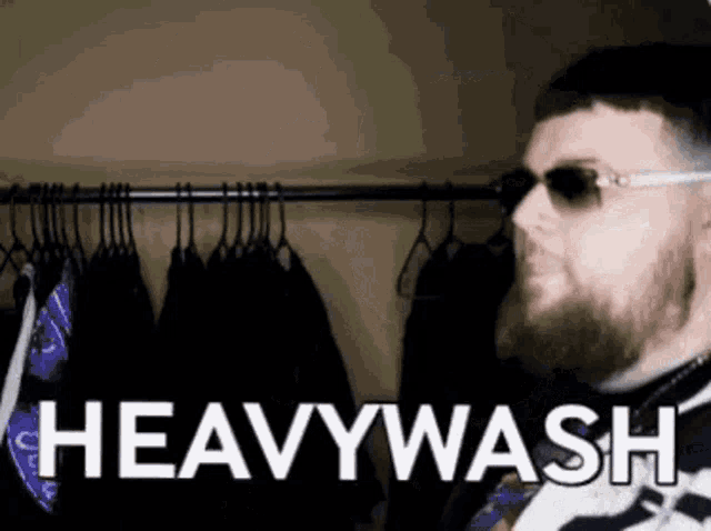 a man wearing sunglasses is standing in front of a rack of clothes with the words heavywash written on it
