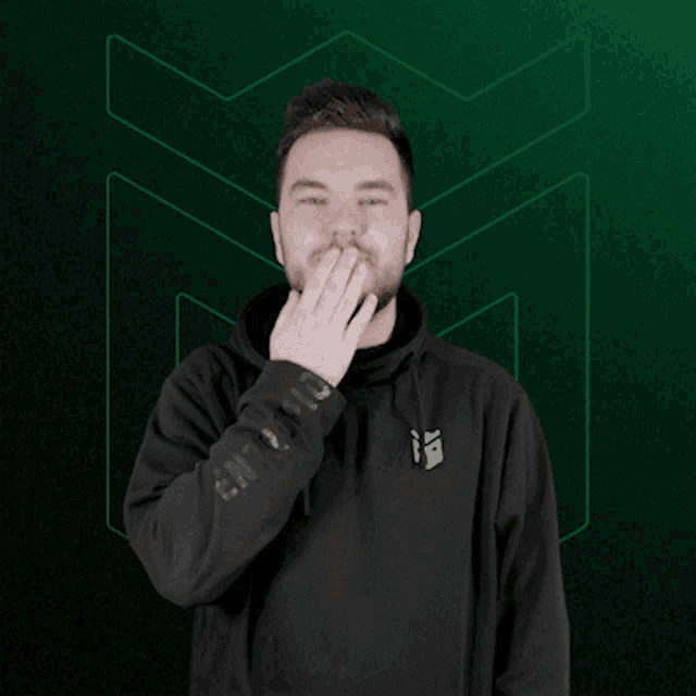 a man wearing a black puma hoodie waves his hand in front of a green background