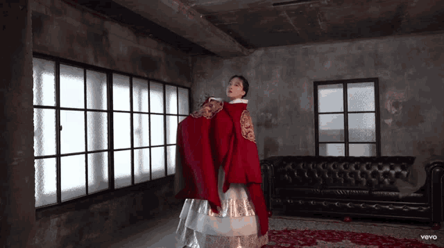 a woman in a red dress is standing in a room with a couch