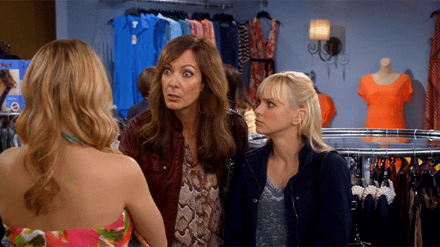 three women are standing in front of a clothing rack with a sign that says ' a ' on it