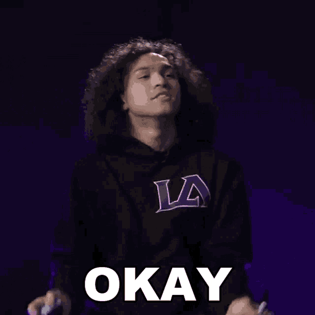 a man with curly hair wearing a black la hoodie says okay