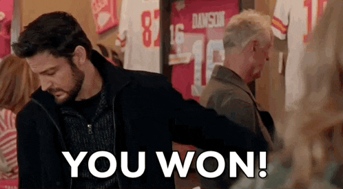 a man with a beard is standing in front of a wall with jerseys hanging on it and says `` you won '' .