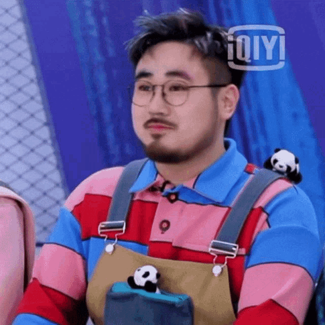 a man with a beard and glasses is wearing overalls and a pink and blue shirt .