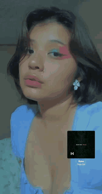 a woman wearing a blue top and earrings has a picture of a song on her chest