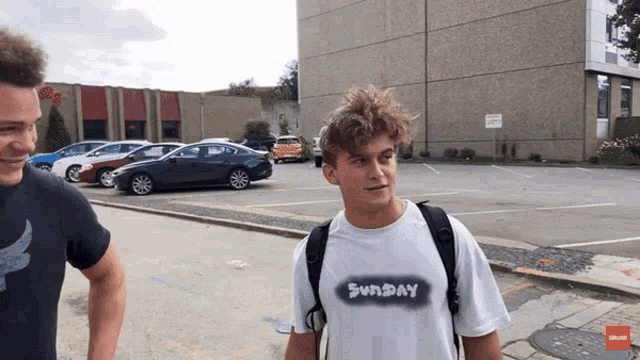 a man wearing a sunday t-shirt is standing next to another man