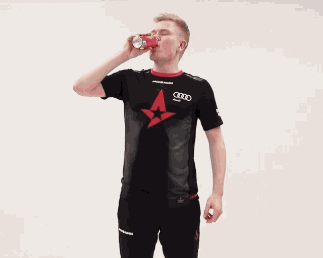 a man wearing a black shirt with an audi logo on it drinks from a red can