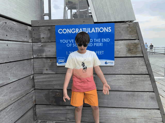 a boy wearing sunglasses stands in front of a sign that says congratulations