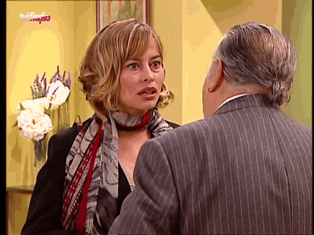 a woman in a scarf is talking to a man in a suit with the word halfagio on the bottom left