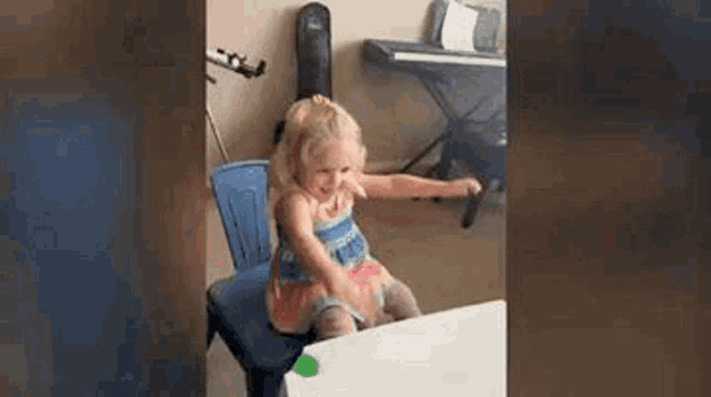 a little girl is sitting at a table with her arms outstretched and a piano in the background .