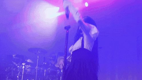a woman singing into a microphone on a stage with purple lights behind her