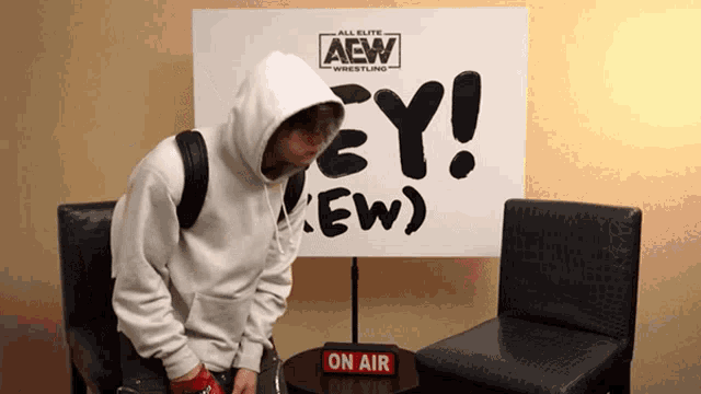 a man in a white hoodie is standing in front of a sign that says aew wrestling