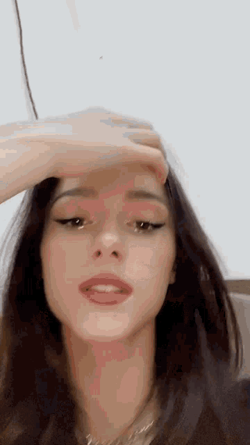 a woman is holding her hand to her forehead and looking at the camera .
