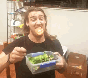 a man with long hair is holding a plastic container with lettuce and tomatoes in it