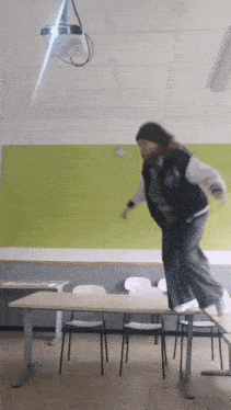 a person jumping over a table in a classroom with a projector in the background