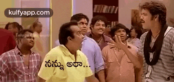a group of men are standing in a room talking to each other and one of them is wearing a yellow shirt .