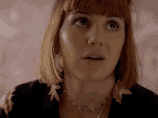 a close up of a woman 's face with a surprised look on her face . she is wearing a necklace .