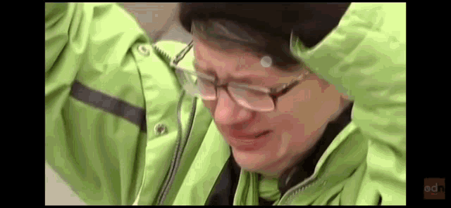 a man wearing glasses and a green jacket crying