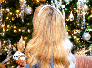 a woman with long blonde hair is holding a phone in front of a christmas tree